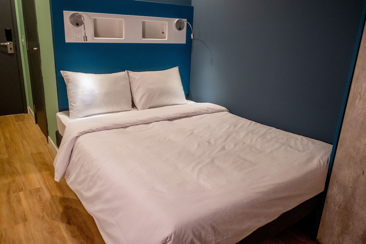 A neatly made bed with white linens in a room with a blue accent wall and a wooden floor.