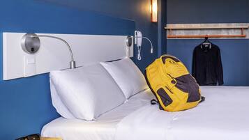 Ein Hotelzimmer mit einem Bett, einem Nachttisch mit Lampe, einem hängenden Telefon und einem Kleiderhaken mit Jacke.