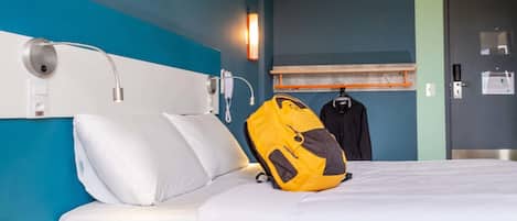 A hotel room with a bed, a bedside table, a wall-mounted phone, and a coat rack with a jacket.