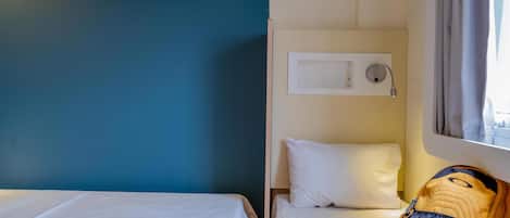 A hotel room with two beds, a window with curtains, a wall-mounted air conditioning unit, and a backpack on the floor.
