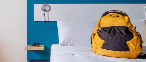 Una cama con ropa de cama blanca, una pared azul y una mochila negra y amarilla sobre la cama.