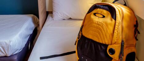 A single bed with white bedding, a small table, and a yellow backpack on the bed.