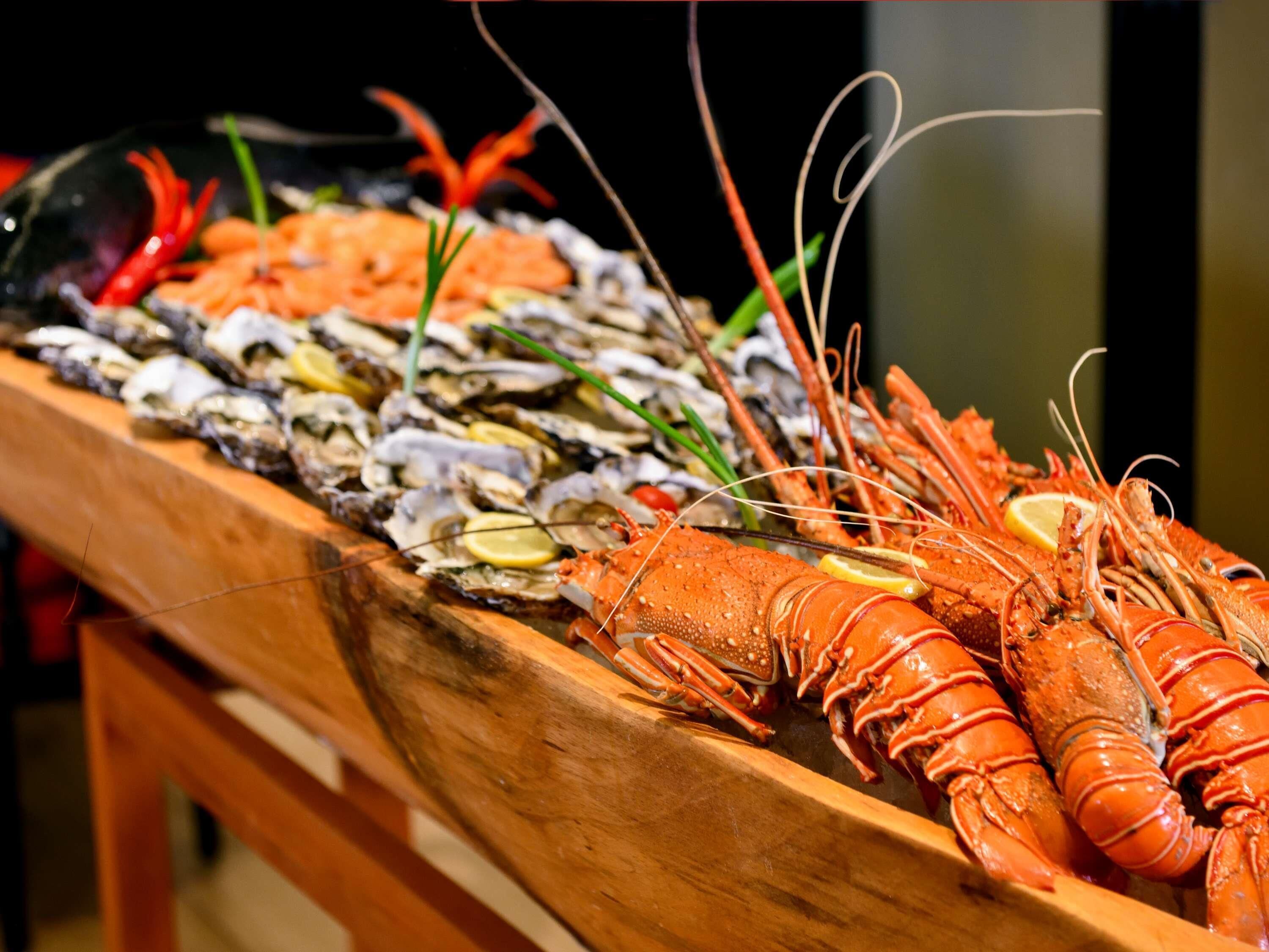 A wooden serving board with seafood, including lobsters and oysters.