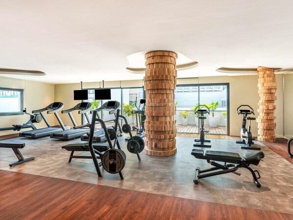 Un gimnasio con cintas de correr, máquinas de pesas y una gran columna de madera.