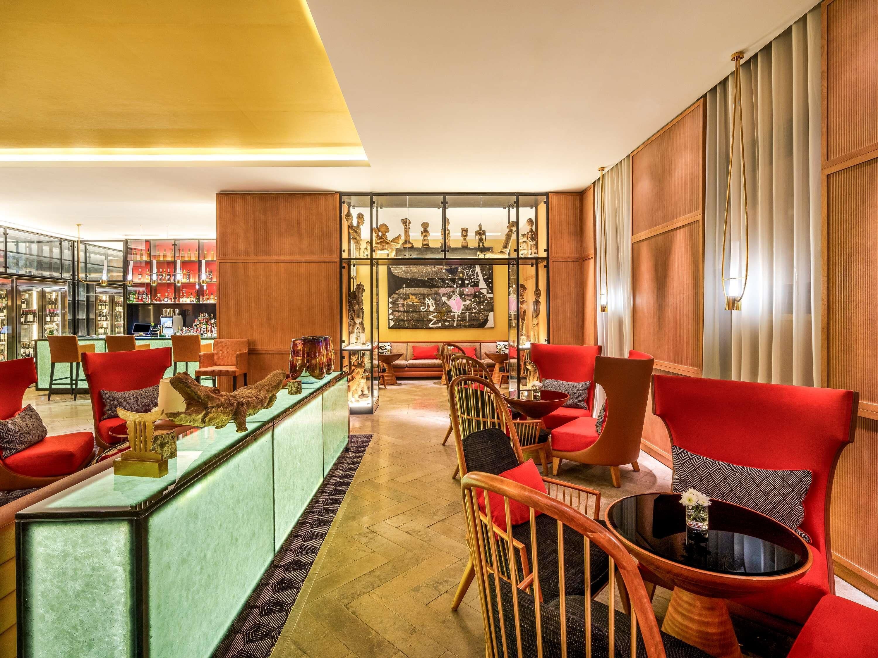 A bar area with red chairs, a glass display case with decorative items, and a seating area with red sofas and wooden chairs.