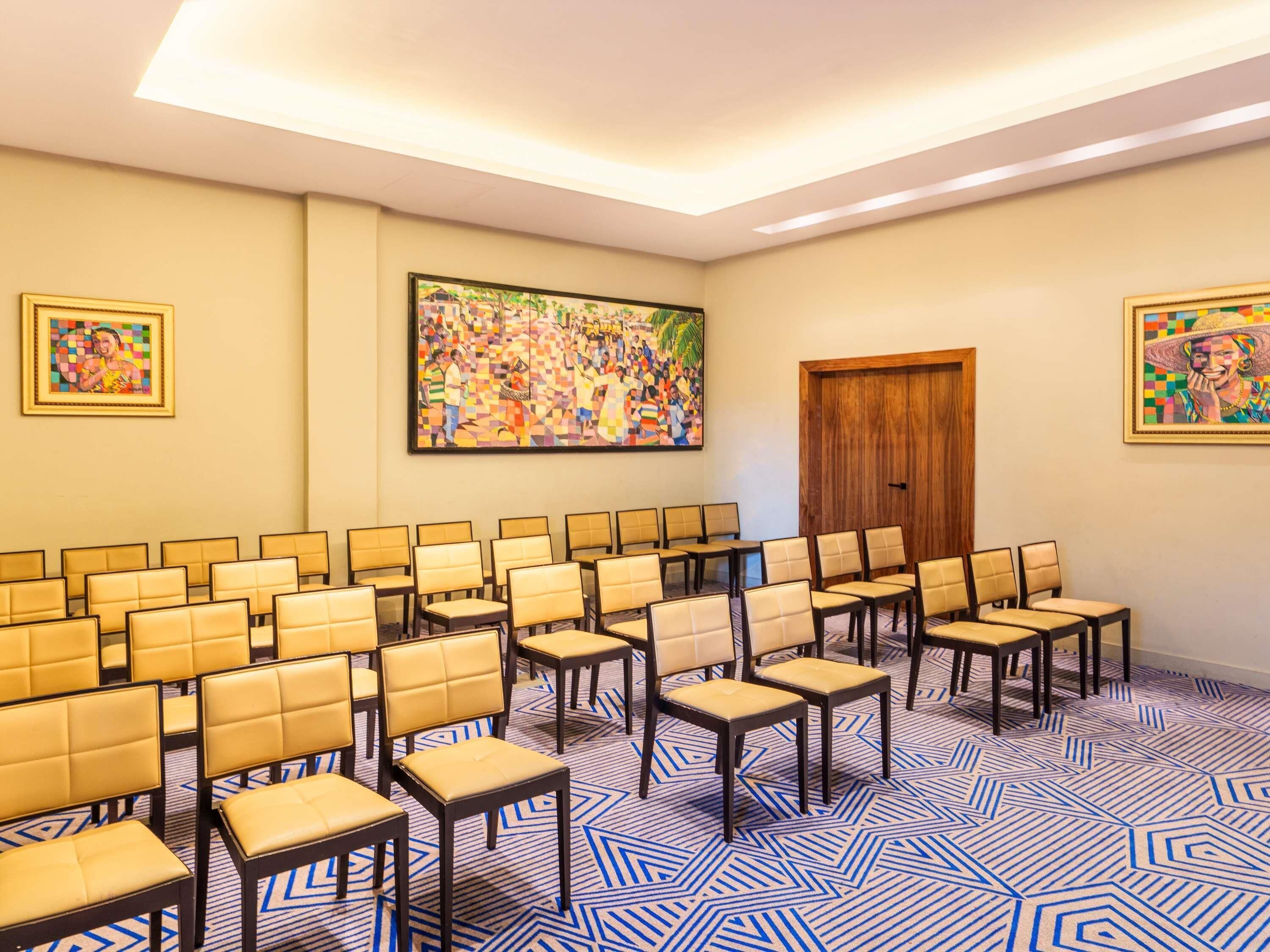 A conference room with rows of chairs, a wooden door, and two framed artworks on the walls.