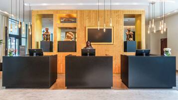 A reception area with three black reception desks, a wooden wall with framed artwork, and modern pendant lighting.