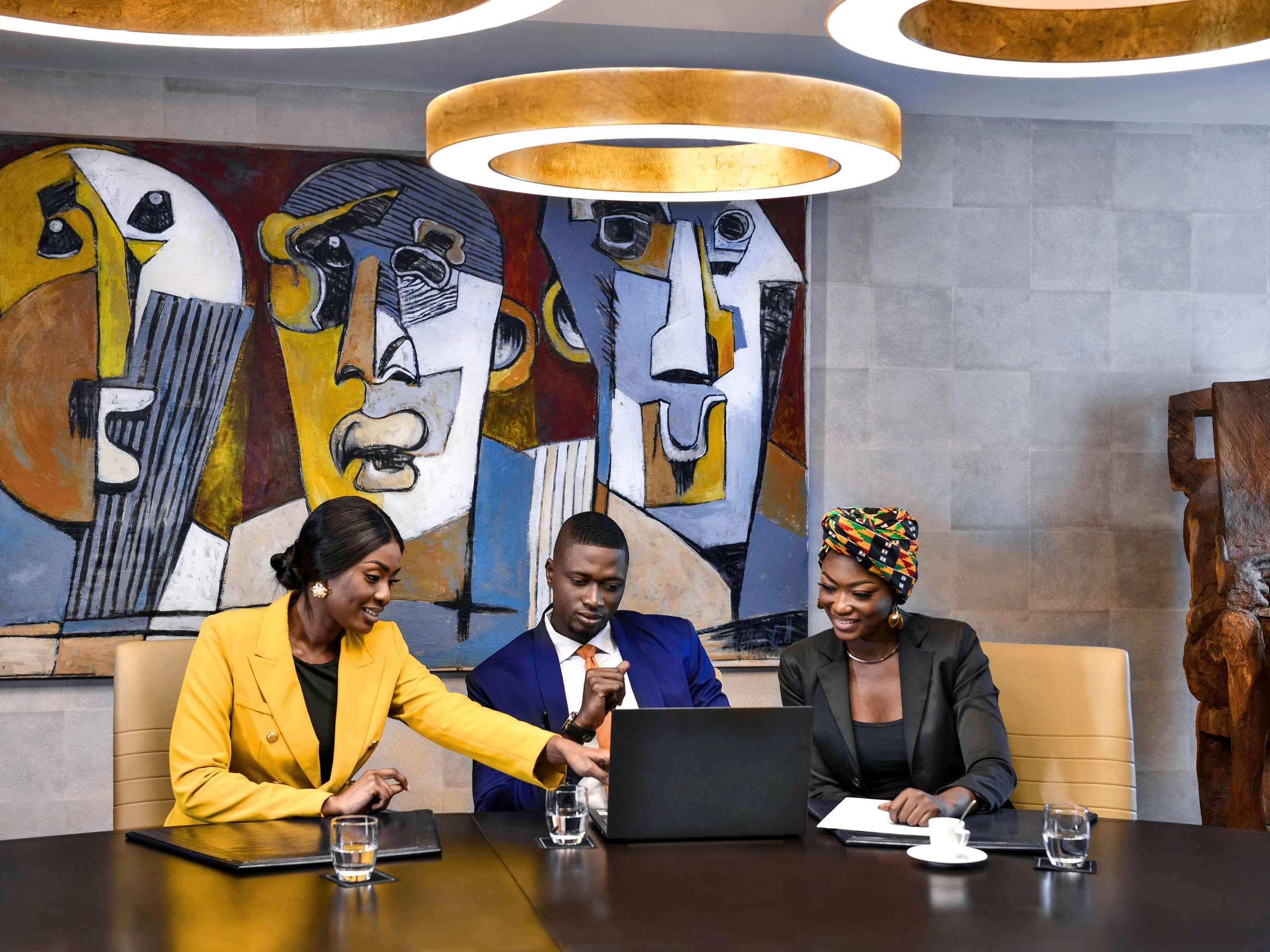A meeting room with a modern design, featuring a large abstract painting on the wall, a round table, and a laptop.