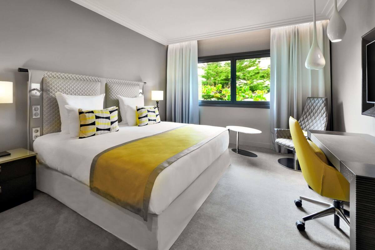 Ein Hotelzimmer mit Bett, Schreibtisch, Stuhl, Fenster mit Blick auf Grünflächen und einem Fernseher.