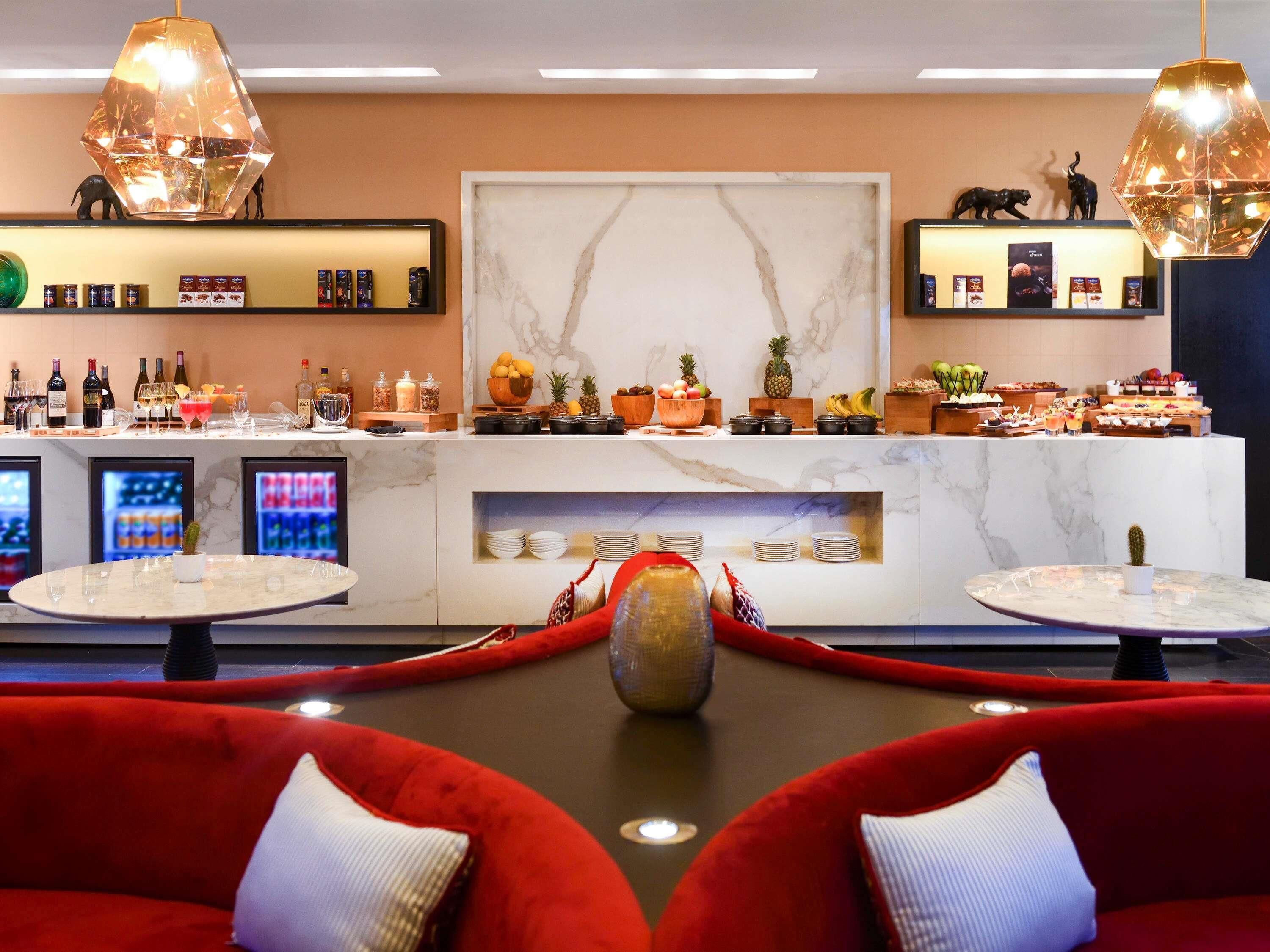 Un hall de hotel con una recepción de mármol, una estación de café y zonas de estar rojas.