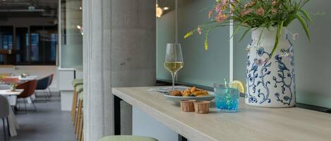 A bar area with a wooden counter, a vase with flowers, a glass of white wine, and a blue drink with ice.