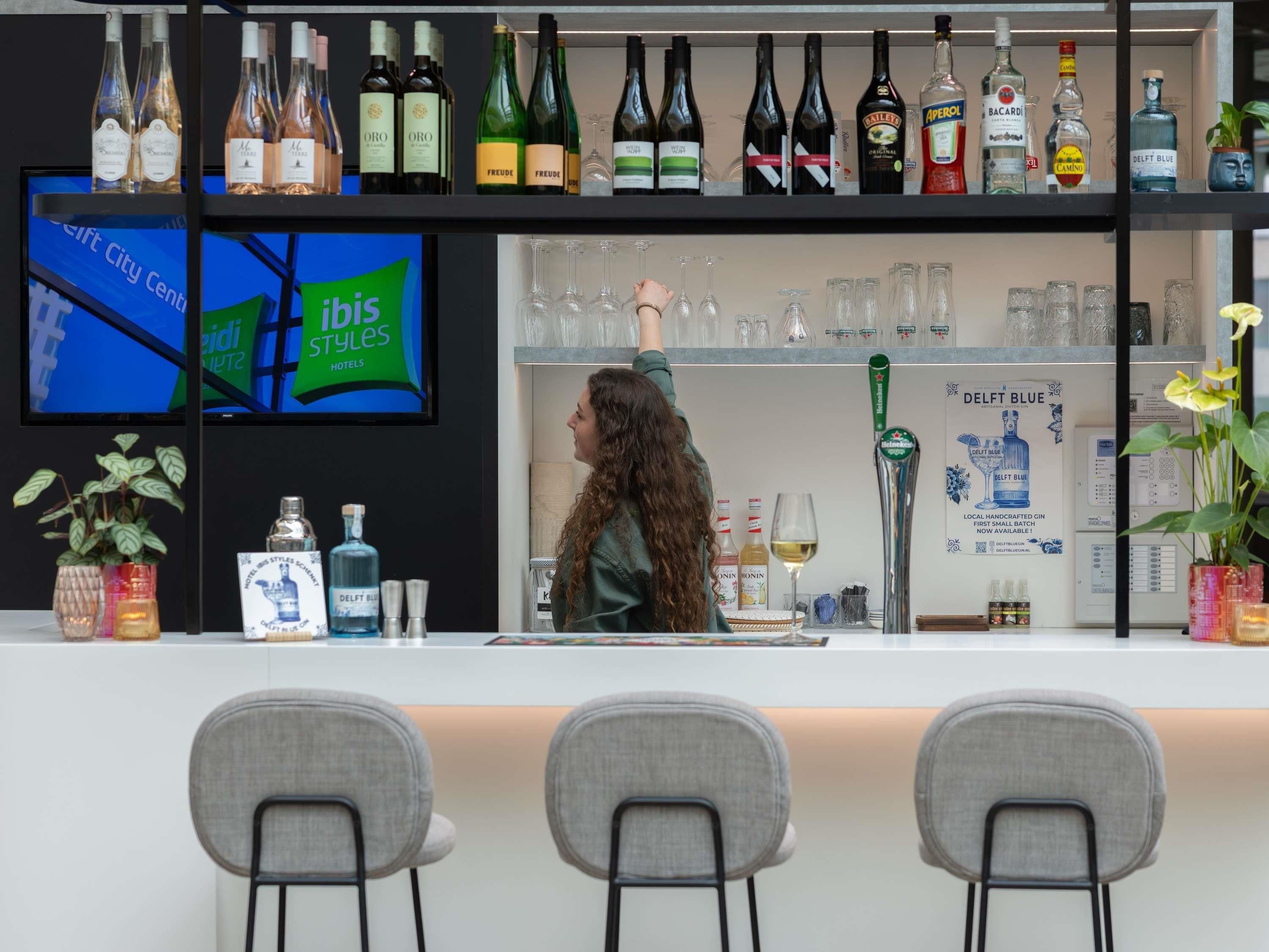 A bar area with a variety of liquor bottles, a television screen, and a bartender.