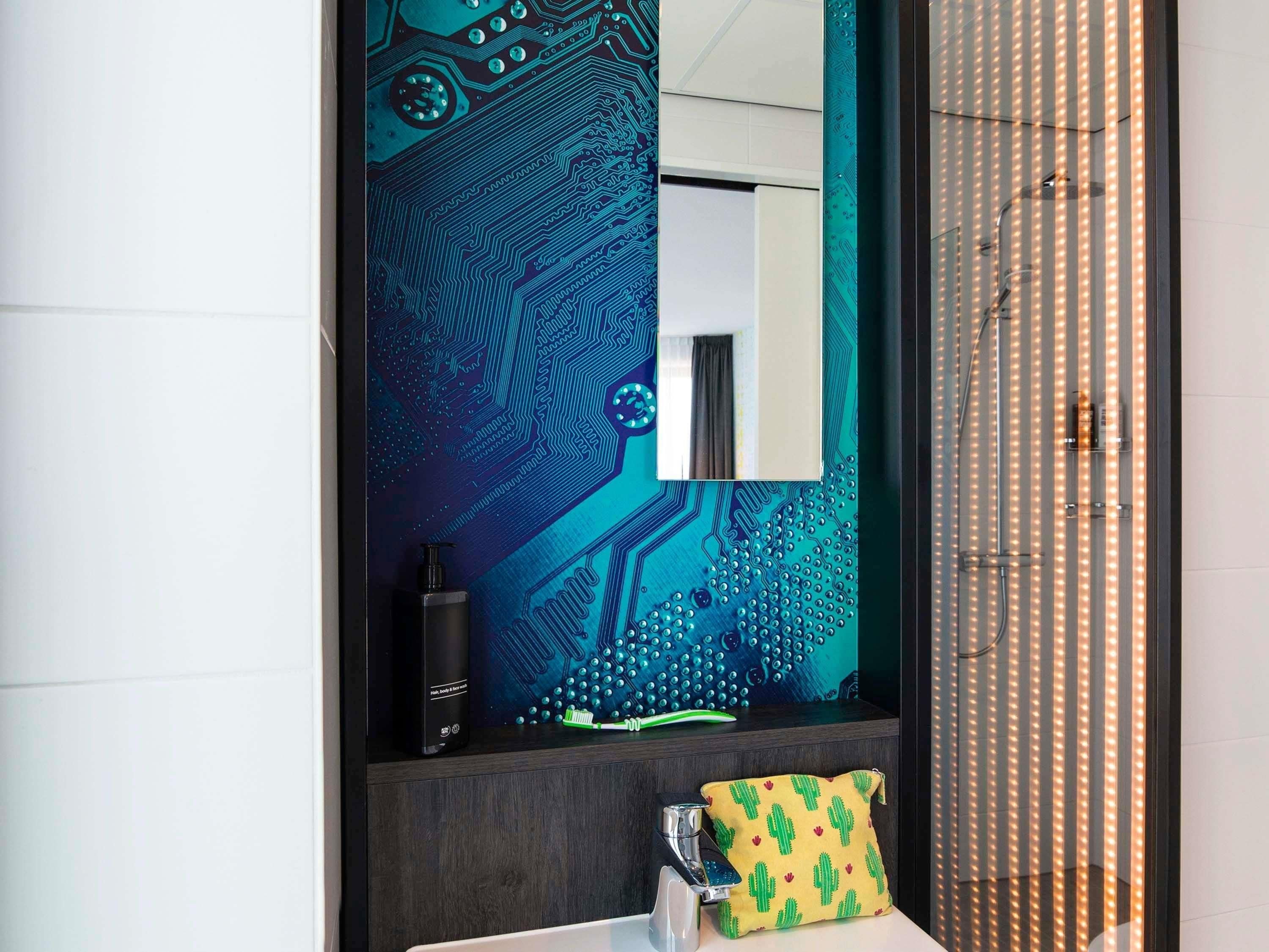 Un baño con espejo, lavamanos, grifo, dispensador de jabón y toalla con estampado de cactus.