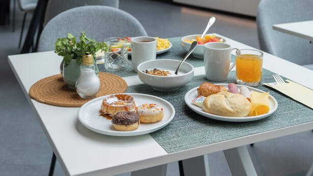 Un espace repas moderne, doté de tables, de chaises et offrant un choix varié d’aliments pour le petit-déjeuner.