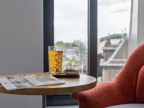 Ein Tisch mit einem Glas bernsteinfarbener Flüssigkeit, einer kleinen Schale Schokolade und einer Zeitung.