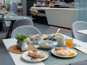 A breakfast setting with a variety of pastries, a coffee cup, and a glass of orange juice. - ibis Styles Delft City Centre (Delft)