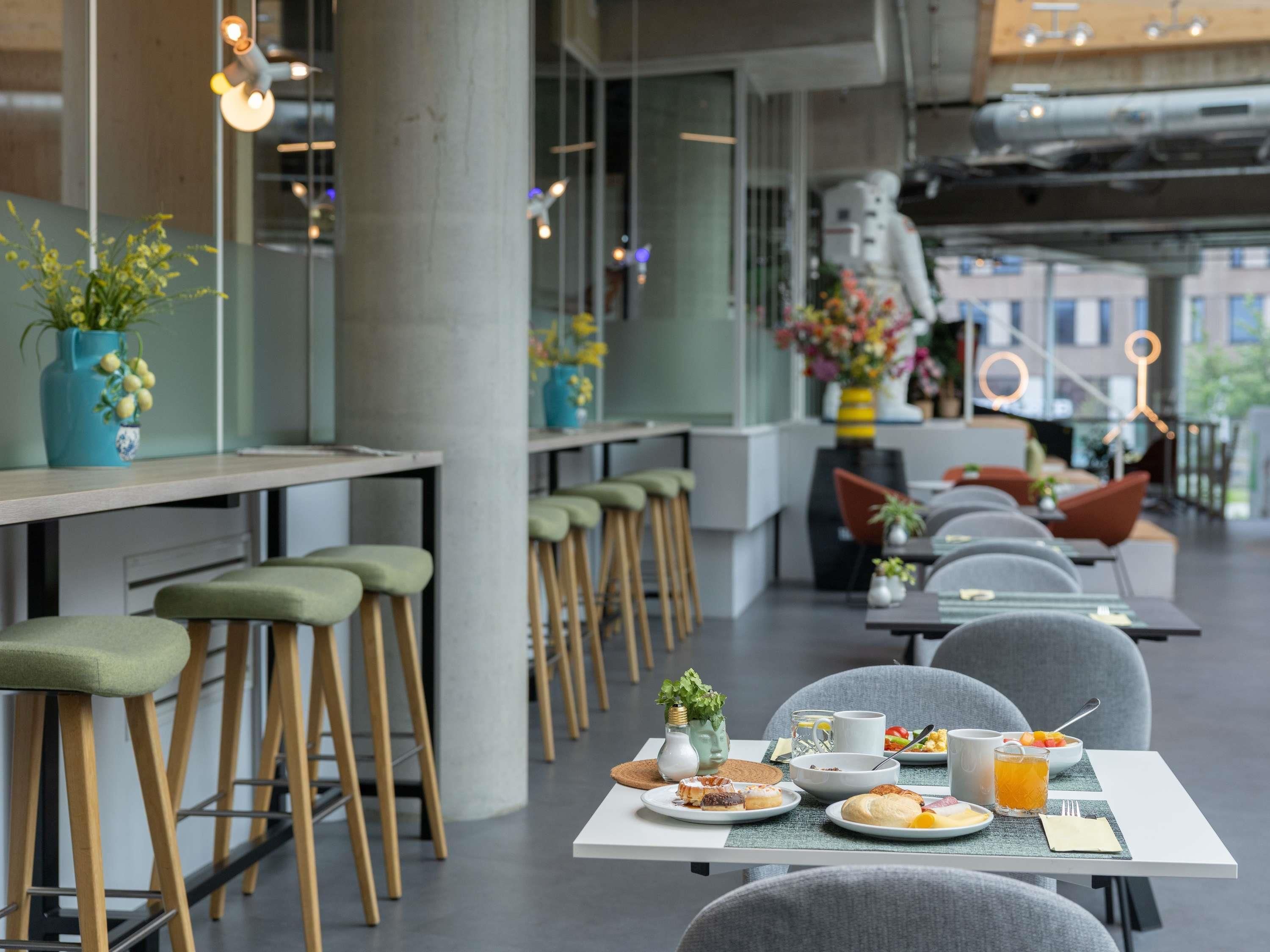 A modern dining area with high tables, bar stools, and a variety of breakfast items.
