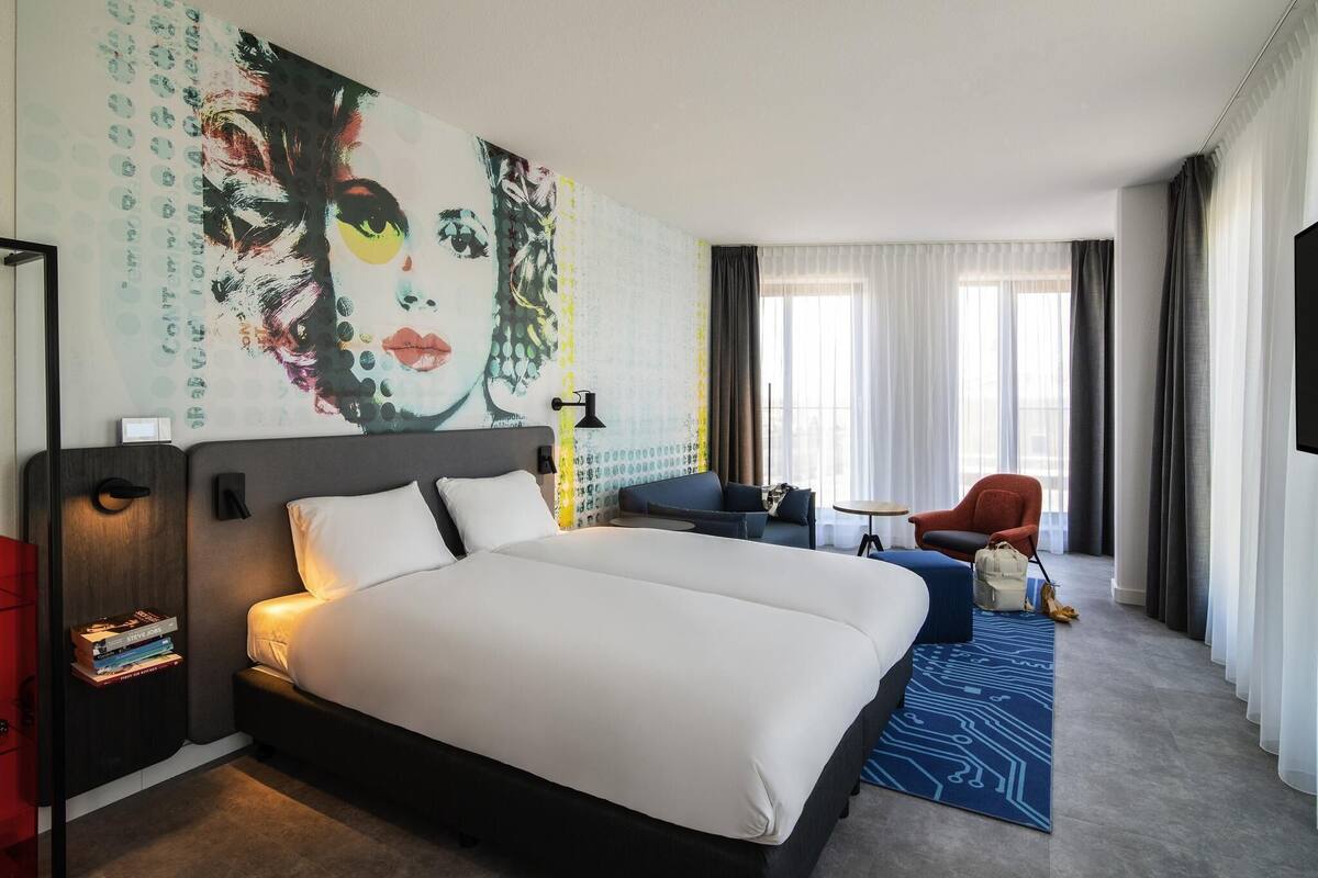 Ein Hotelzimmer mit einem großen Bett, einem Schreibtisch, einem Stuhl, einem Fernseher und einem Fenster mit Vorhängen.