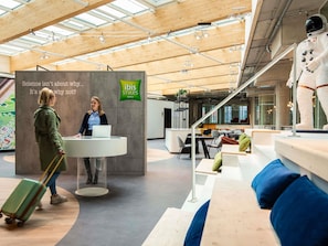 Moderni hotellin aula, jossa on vastaanottotiski, lasiseinä ja suuri kyltti.