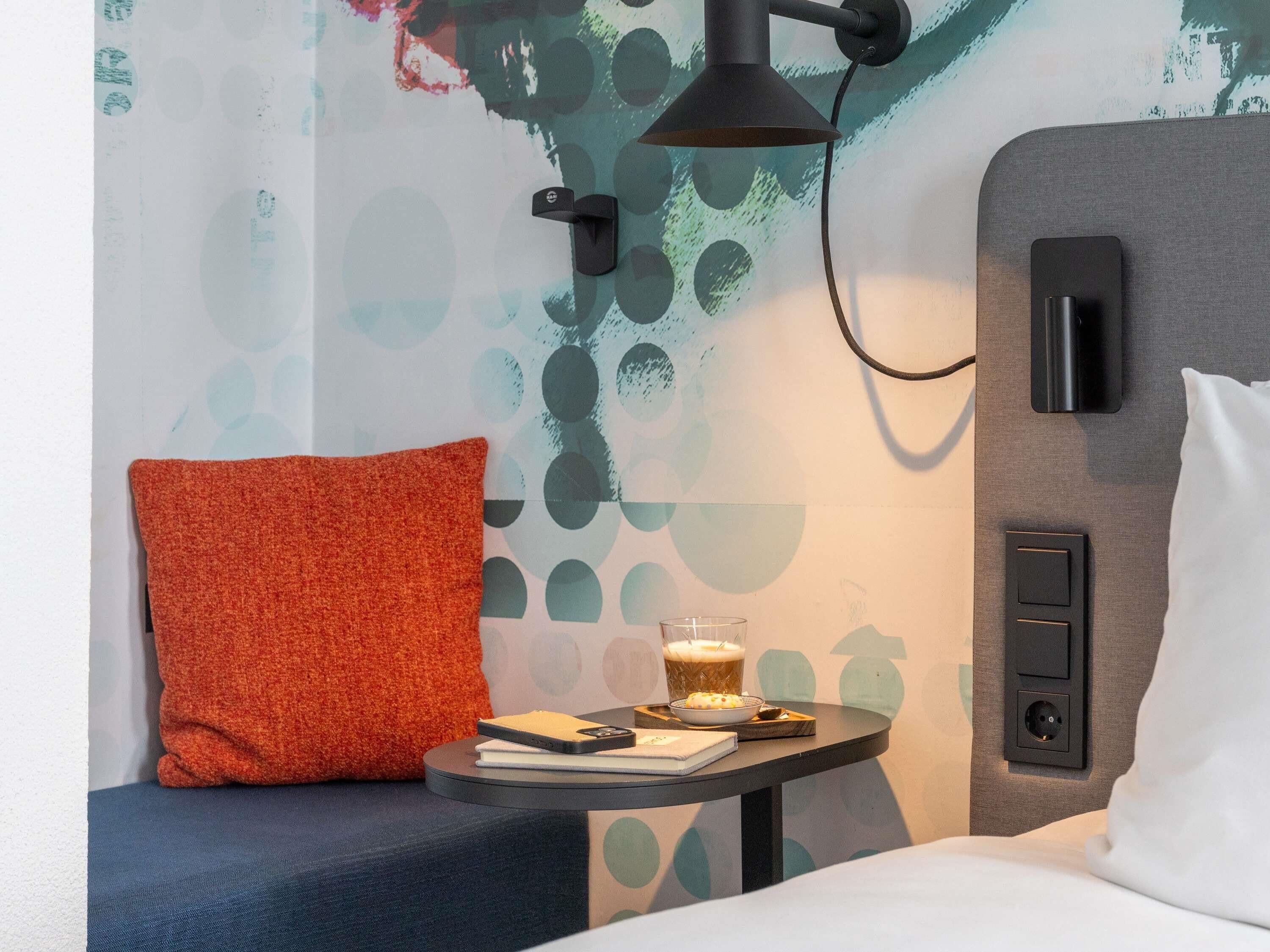 Une chambre d’hôtel avec une table ronde, un coussin rouge, un verre de bière, un carnet et un téléphone intelligent.