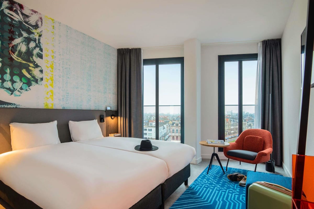 Quarto de hotel com cama grande, escrivaninha, cadeira e vista para a cidade.