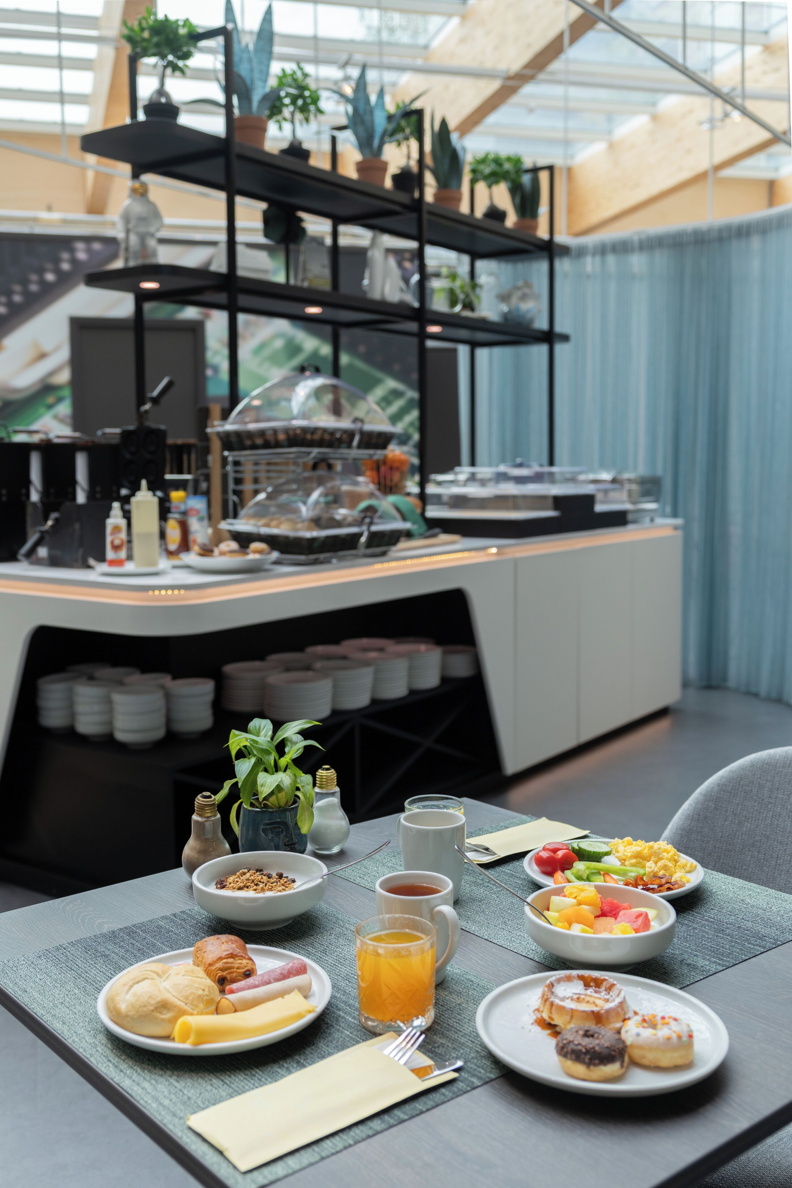 Un desayuno preparado con platos de comida, una cafetera y una estantería con plantas en macetas.
