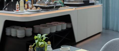 Un desayuno preparado con platos de comida, una cafetera y una estantería con plantas en macetas.