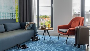 Une chambre d’hôtel moderne avec un canapé, un fauteuil rouge, une petite table avec un vase et une valise.
