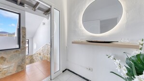 Un baño moderno con una pared de acento de piedra, un espejo redondo y un estante de madera con artículos de aseo.
