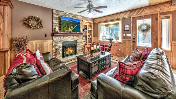 Una sala de estar acogedora con chimenea, sofás de cuero y un televisor montado en la pared.