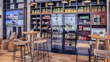 A modern shop interior with wooden shelves stocked with snacks, a refrigerated section, and a television displaying a cityscape.