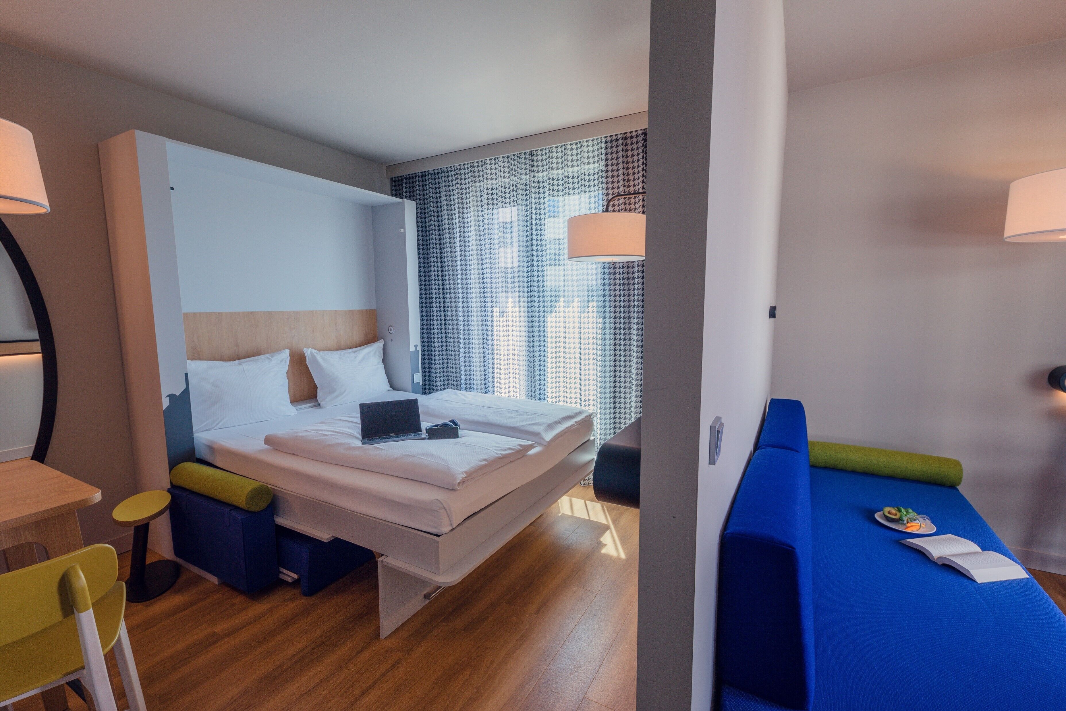 A modern hotel room with a bed, bedside table, and a small desk area.