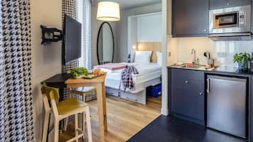 A compact hotel room with a kitchenette, a bed, a dining area, and a TV.
