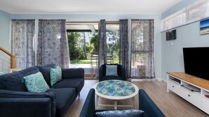 A modern living room with a sofa, armchair, and coffee table, a TV, and a sliding glass door leading to an outdoor area.
