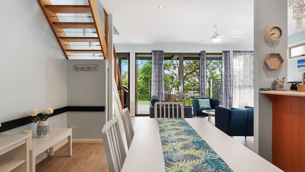 A modern living room with a long white table, blue sofas, and a view of the outdoors through large windows.