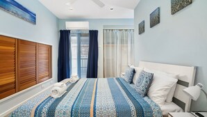 A bedroom with a large bed, a wooden wardrobe, an air conditioning unit, and a view of the city through the window.