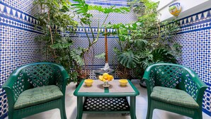 A small patio with two green chairs, a table with a bowl of fruit, and potted plants. - CHIC-ALAMEDA (Sevilla)