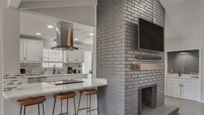 Une cuisine moderne avec une cheminée en briques, des meubles blancs et un grand îlot central doté de tabourets de bar.