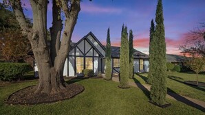 Une maison moderne avec un grand arbre dans le jardin et une pelouse bien entretenue.
