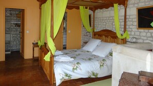 A four-poster bed with a floral bedspread and green curtains, a stone wall, and a wooden ceiling. - Gite du Manoir des Roches (SAIRES)