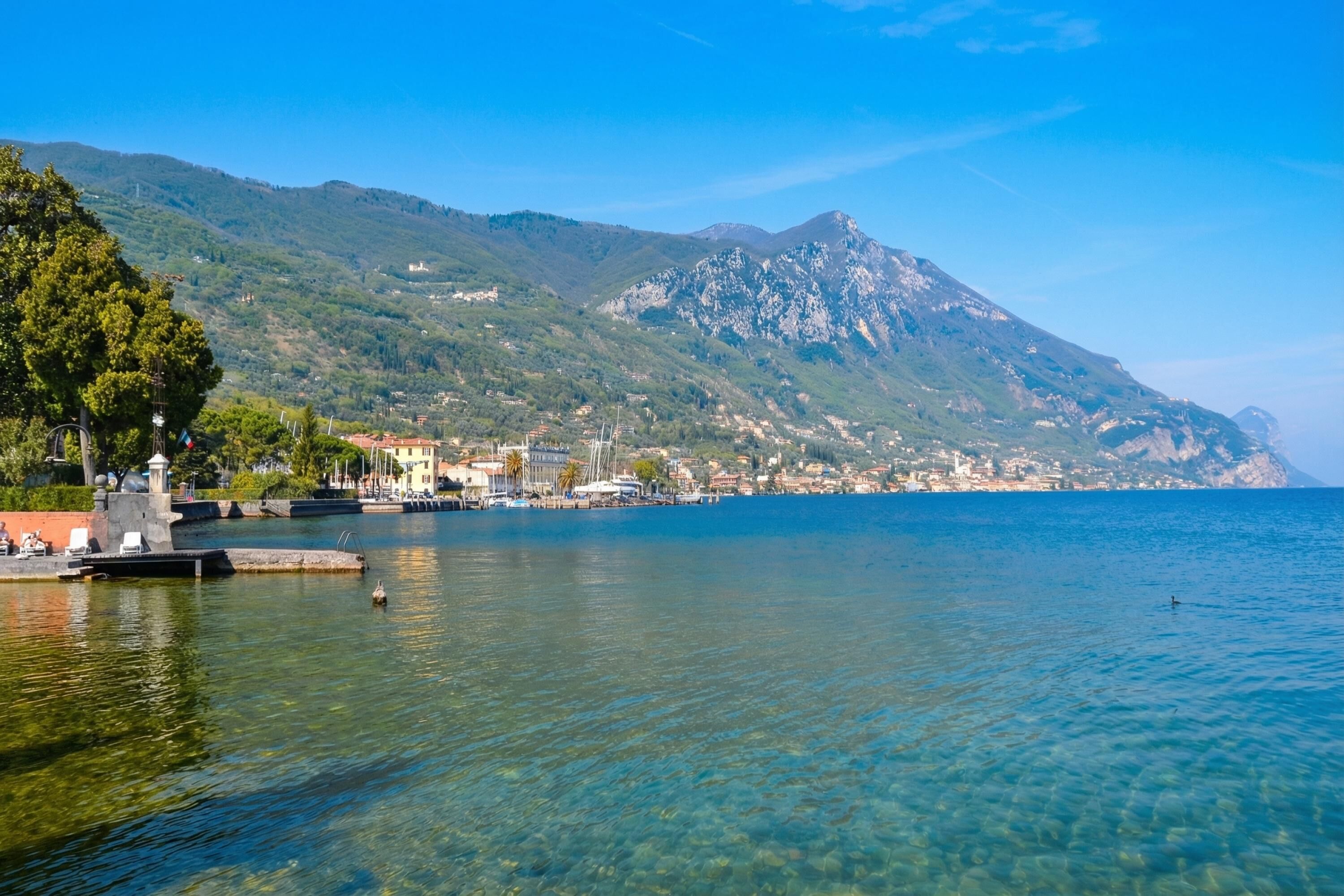 Un pueblo costero con aguas transparentes, un puerto deportivo y montañas al fondo.