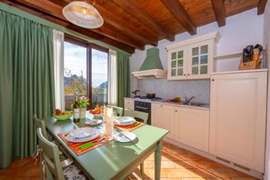 Ein Essbereich mit Tisch für zwei, eine Küche mit weißen Schränken und Blick auf Berge durch das Fenster.