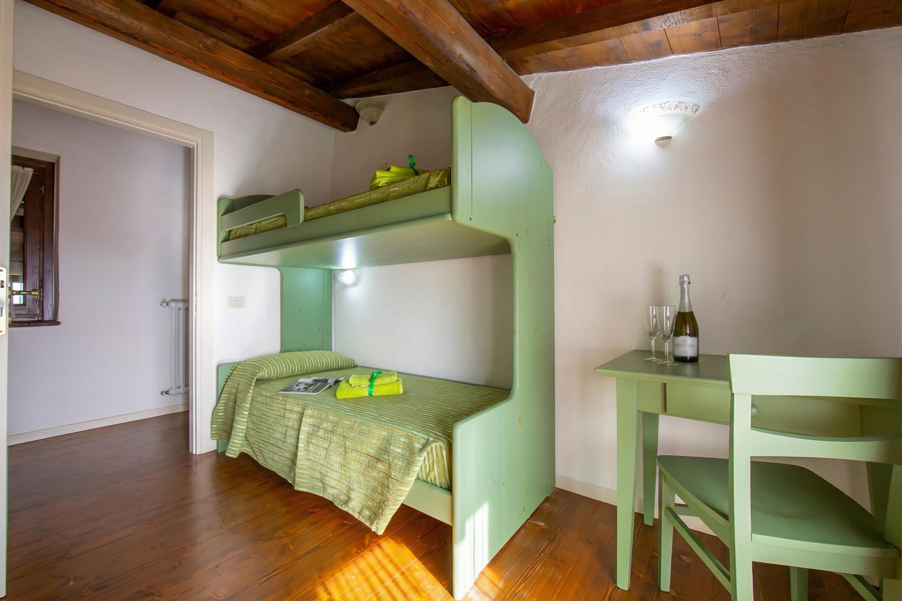 Une pièce avec un lit superposé, une petite table avec deux verres et une bouteille, et un plancher en bois.