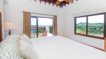 A hotel room with a large bed, a ceiling fan, and a view of a balcony with outdoor furniture.