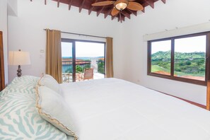 A hotel room with a large bed, a ceiling fan, and a view of a balcony with outdoor furniture.