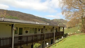 A two-story building with a balcony, a wooden fence, and a grassy yard. - No 6 at Dolgoch Falls Cottages (Bryncrug)
