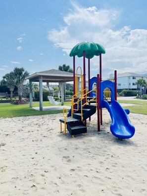 A playground with a blue slide, yellow and red climbing structures, and a covered seating area.