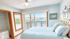 Ein Schlafzimmer mit einem großen Bett, einem Deckenventilator, Blick auf ein Gewässer und einem Balkon.