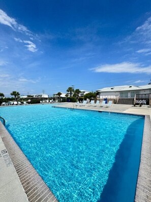 A swimming pool with clear blue water, surrounded by lounge chairs and a covered area.