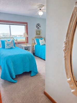 A bedroom with two beds, a ceiling fan, a window with a view, and a clock on the wall.